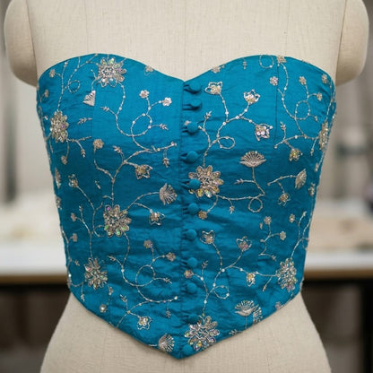 A turquoise blue strapless corset bustier with intricate gold floral embroidery and button closures, displayed on a beige fabric dress form.