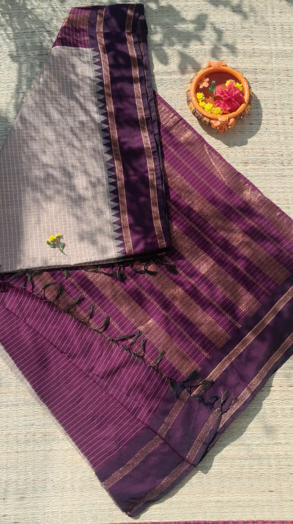 Beige saree with a purple border and pallu with decorative item on a light fabric background